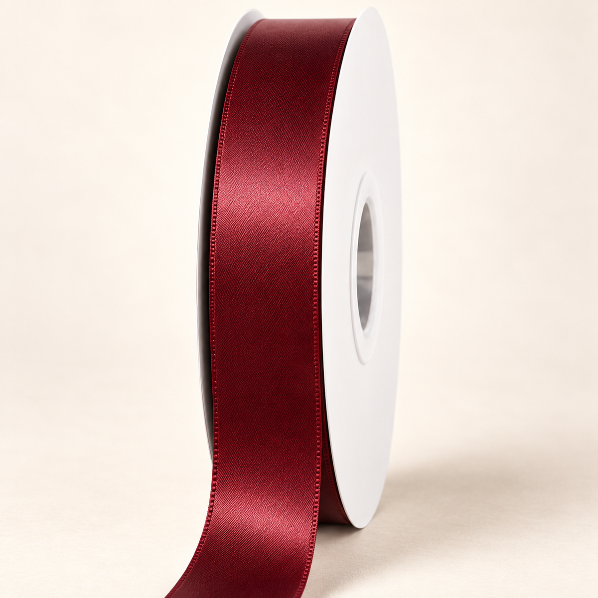 Burgundy 22 mm double-faced satin ribbon on a white roll against an ivory background